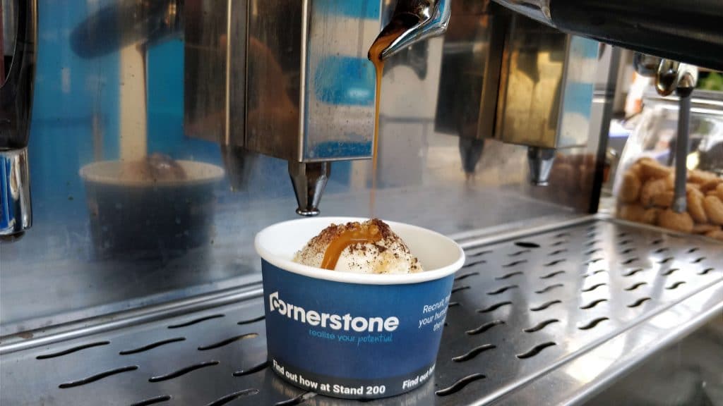 Barista pouring butterscotch sauce onto ice cream in a Cornerstone promo paper cup